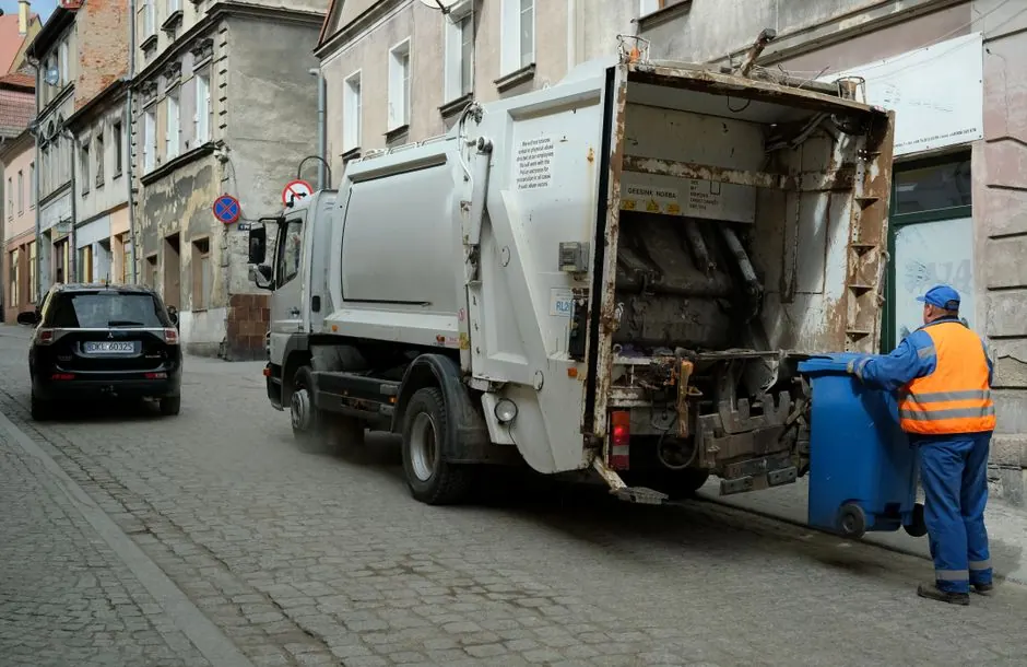 City street scene with garbage truck and worker handling waste bin.
